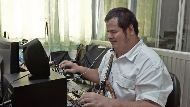 เอกลักษณ์ ใส่หูฟัง นั่งอยู่หน้าคอมพิวเตอร์ตั้งโต๊ะในห้องฝ่ายไอซีที สถาบันคนตาบอดฯ