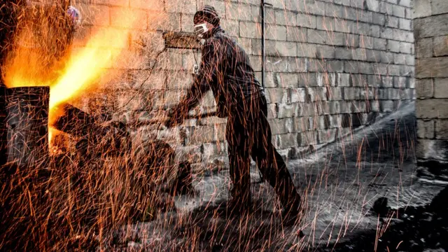 Күнөскана иштеткен фермер. Жашылча-жемиштер өскөн жайды ысык темпаратурада кармоо үчүн үчүн от жагып жатат.