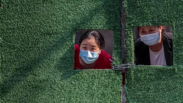 上海某住宅小區內兩位被封控禁足的女士從柵欄的孔洞窺探小區外情況（25/4/2022）