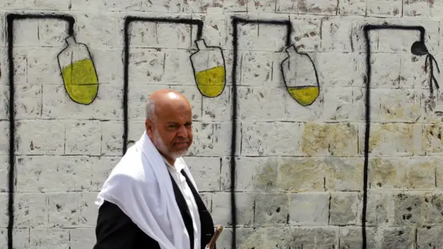 A Yemeni walks past graffiti depicting intravenous drips on a wall in Sanaa, Yemen (23 May 2017)