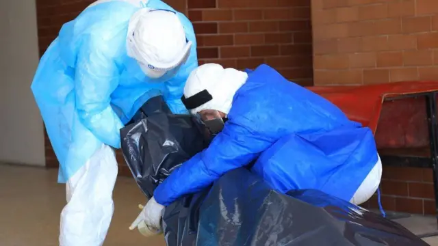 Personal de salud con un muerto en una bolsa plástica.