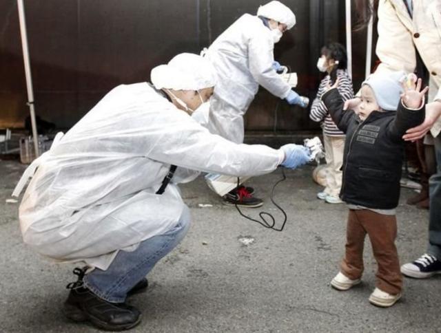 2011年福岛核事故后，身穿防护衣的工作人员为儿童检查辐射迹象。