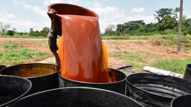 Une femme verse un récipient d'huile de palme dans un baril à Divo (Côte d'Ivoire)