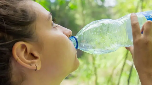 Mujer toma agua en botella de plástico.