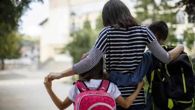Madre lleva a niños a al escuela.