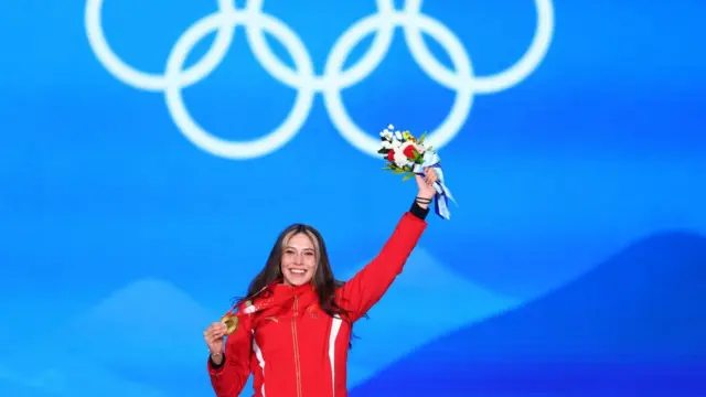 Eileen Gu en el podio con la medalla de oro y un ramo de flores
