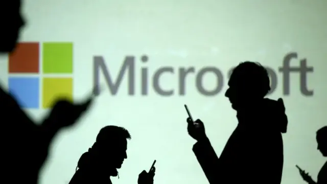 Pessoas usam celular com painel da Microsoft ao fundo