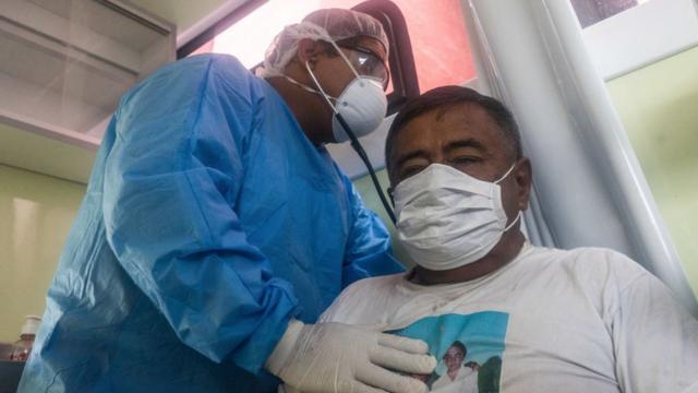 Un médico vistiendo equipo de protección personal atiende a un paciente en Perú.