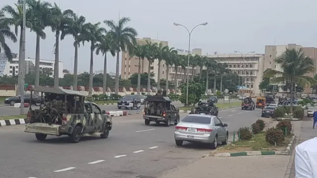 Armed security inside vans during Protesters wey dey carry sign boards