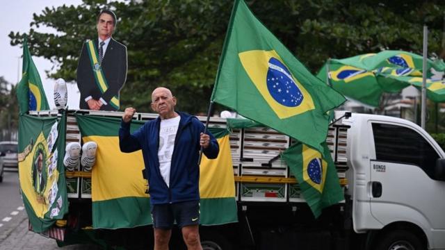Apoiador do presidente Jair Bolsonaro carregando bandeira do Brasil,betmotion linkedinfrente a um pequeno caminhão também decorado com bandeiras, bonecos infláveisbetmotion linkedinLula vestidobetmotion linkedinpresidiários e uma imagembetmotion linkedinBolsonarobetmotion linkedinpapelão