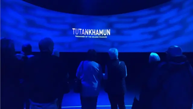 الزوار يقفون أمام شاشة كتب عليها توت عنخ آمون