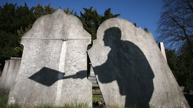 La sombra de un obrero de un cementerio proyectada sobre unas lápidas