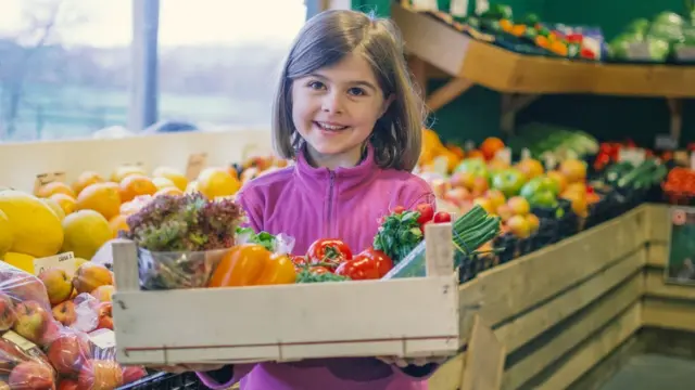 Niña con caja de verduras.