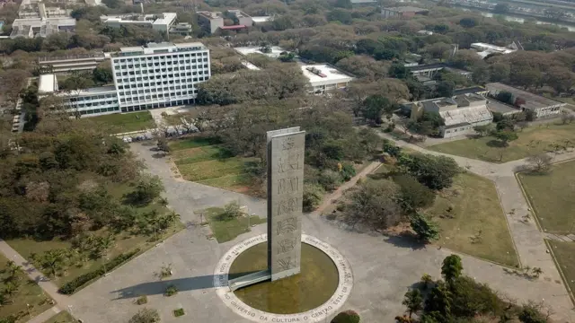 Foto colorida mostra vista aérea da Praça do Relógio, uma praça ampla com uma torre moderna no centro
