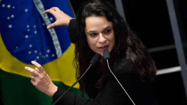 Jurista Janaína Paschoal falando ao microfone,ganhar nas apostas esportivasfrente a uma bandeira do Brasil