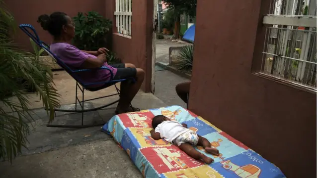 Mujer en sillón sentada, bebé sobre colchón