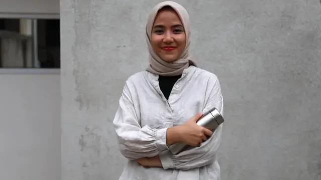 Astri Puji Lestaria stands outside her home in Jakarta holding a re-usable water bottle.