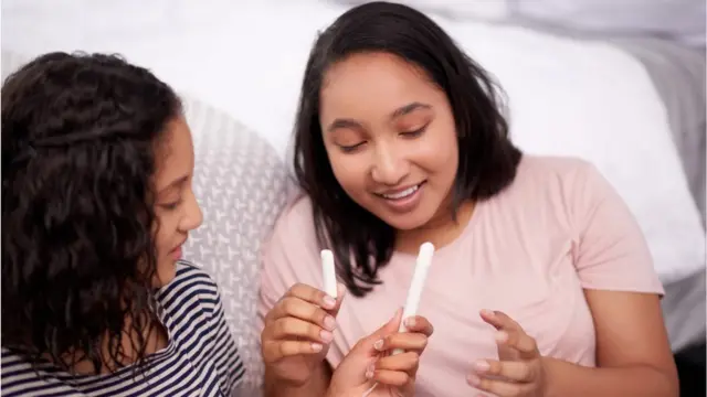 Duas meninas pardas seguram um absorvente interno e conversam