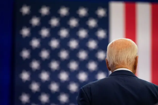Biden de espalda con la bandera de EEUU de fondo