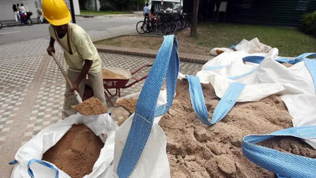Seorang pekerja mengisi gerobak dorong dengan pasir di dekat lokasi konstruksi di Singapura
