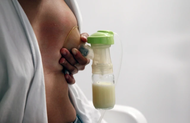 Una mujer sujeta un extractor de leche a su seno, mientras la leche cae en una botella pequeña