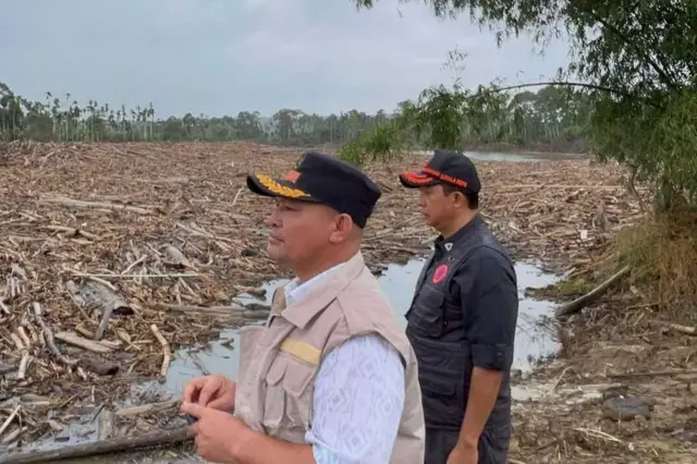 Bupati Aceh Utara Ismail A Jalil (kiri) dan Kepala Badan Nasional Penanggulangan Bencana (BNPB), Letjen TNI Suharyanto (kanan) melihat tumpukan kayu sisa banjir diDesa Geudumbak, Kecamatan Langkahan, Kabupaten Aceh Utara, Senin (15/12/2025).