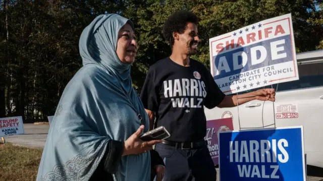 Awet Howard Eyasu, ancien réfugié érythréen, et Sharifa Adde, ancienne réfugiée somalienne, brandissent des pancartes de campagne en Géorgie, le jour des élections américaines.