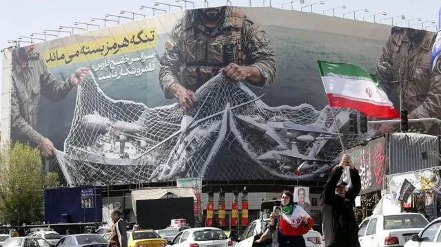 तेहरान में एक बैनर लगा हुआ है जिस पर लिखा है- 'स्ट्रेट ऑफ़ होर्मुज़ बंद रहेगा; पूरी फारस की खाड़ी हमारा शिकारगाह है.' एक सैनिक के हाथ में जाल है जिसमें टैंकर और फ़ाइटर जेट फंसे दिखाई देते हैं