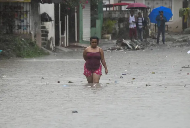 Una mujer con el agua hasta las rodillas camina en una calle inundada en República Dominicana