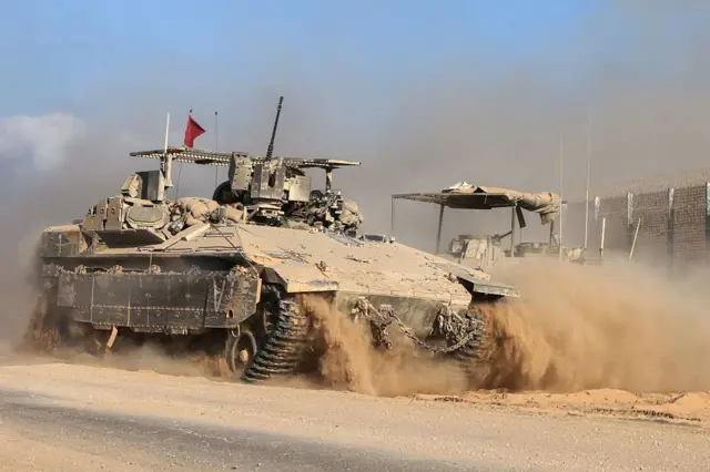 An Israeli military vehicle drives past a border fence amid a cloud of sand and dust