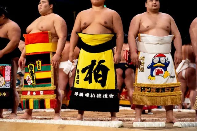 Sumo wrestlers, also known as Rikishi, during the opening ceremony on day two
派手な化粧まわしを着けて土俵に並んだ力士たち