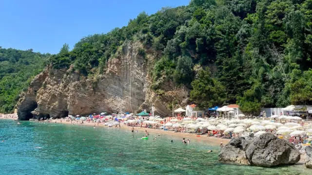 Plaża w Czarnogórze z wysokim półwyspem, czystą wodą i słonecznym niebem.