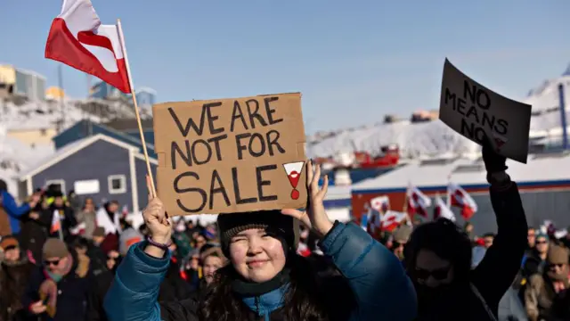 Çok soğuk bir havada yapılan protestoda kadın protestocu "Satılık değiliz" yazılı bir pankart taşıyor. Arkasında ve yanında çok sayıda kişi var.