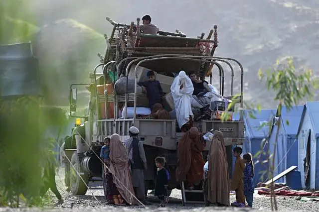 لاری حامل مهاجران. عمدتا زنان و کودکان با وسایل خانه دیده می‌شوند. زنی با چادری سفید در حال پیاده شدن از لاری