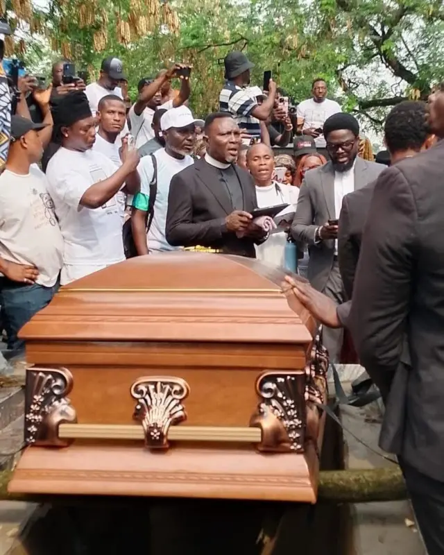 Casket wey pesin wey look like pastor and oda pipo surround.