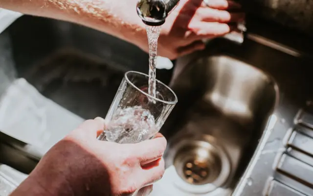 Un hombre llena un vaso con agua en el grifo.