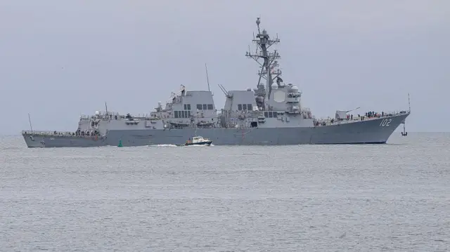 En un mar tranquilo navega un barco de guerra de color gris con el número 102 escrito es letras blancas en su proa.