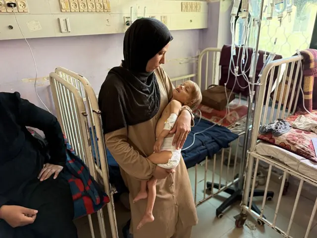 Una mujer con un velo oscuro sujeta y mira con preocupación a una niña de 4 años desnutrida en un hospital de Gaza.
