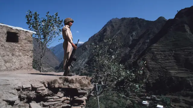 جندي باكستاني يقف على حافة صخرة ويضع بندقيته على الأرض، وينظر عبر خط السيطرة إلى كشمير الخاضعة للإدارة الهندية.