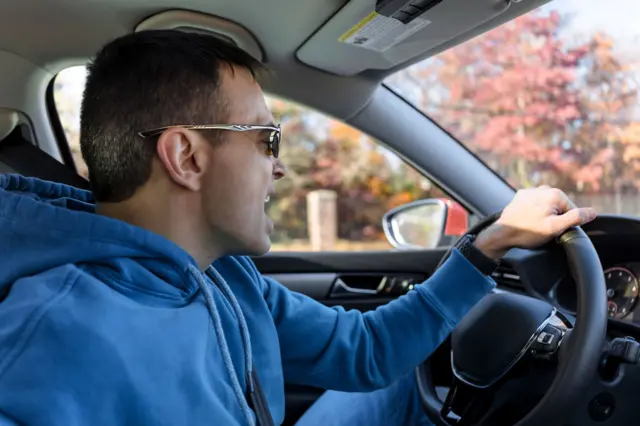 Widok z boku dorosłego mężczyzny śpiewającego w samochodzie podczas jazdy