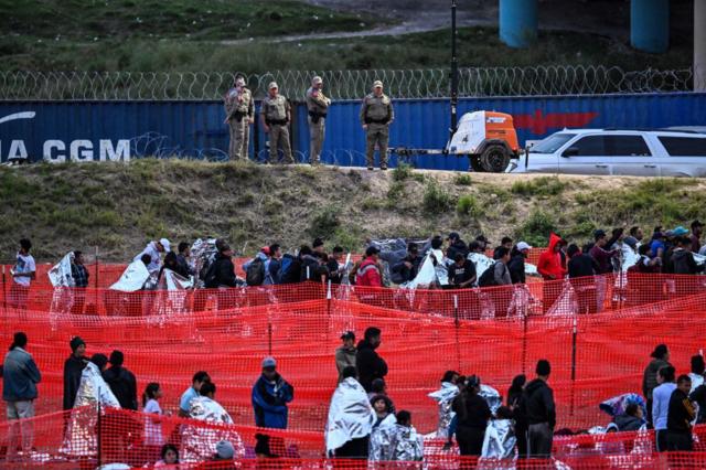 Agentes de Aduanas y Protección Fronteriza hacen guardia mientras los inmigrantes esperan ser procesados ​​en un centro de tránsito de la Patrulla Fronteriza de EE. UU. después de cruzar la frontera desde México en Eagle Pass, Texas, el 22 de diciembre de 2023