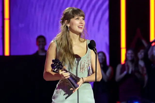 Zdjęcie Taylor Swift z marca 2026 roku. Taylor trzyma nagrodę w ręku i stoi na scenie. 