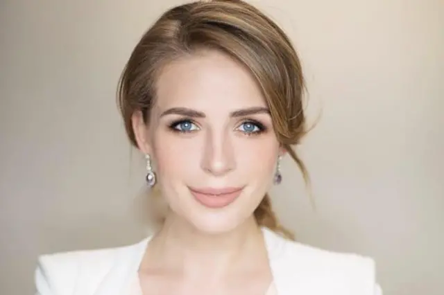 Mulher sorri com o cabelo para trás, vestindo jaqueta branca