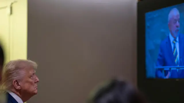 Trump com olhar sério em frente a TV com Lula discursando