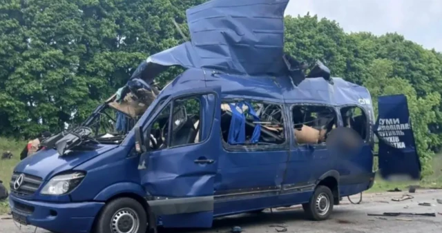 Mavi minibüs saldırı sonrası yol ortasında yamru yumru bir halde duruyor. Pencereleri patlamış kapıları açık.