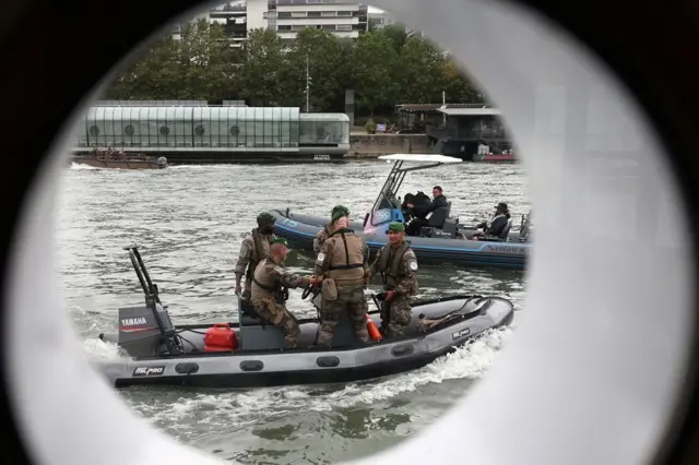 Des membres des forces armées françaises à bord d'un bateau à moteur sont vus à travers le hublot d'un bateau sur la Seine alors qu'ils patrouillent avant la cérémonie d'ouverture des Jeux olympiques de Paris 2024 à Paris.