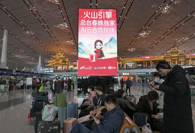 火車站裡很多人背著大包小包，背景板上有一個豆包宣傳畫。