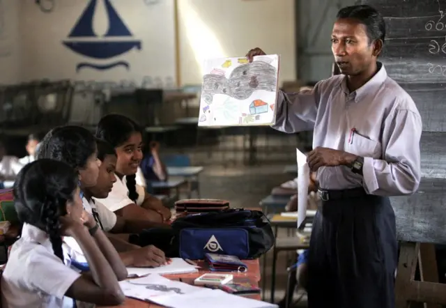 පන්ති කාමරයේ සිටින දරුවන් පිරිසකට උගන්වන ගුරුවරයෙක්. 