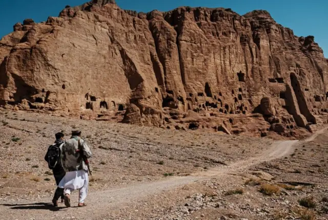 رجلا في الزي المحلي يصطحب آخر في أرض جبلية قاحلة خاوية من أي معالم