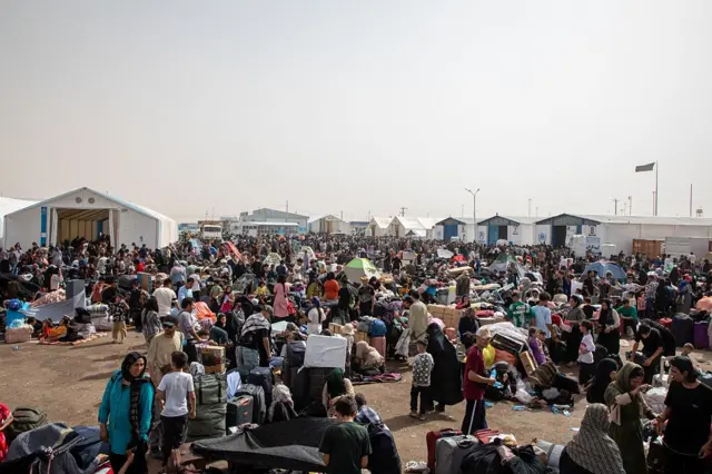 انبوهی از مهاجران دیده می‌شود. شمار زیادی از آنها زن و کودک هستند که با وسایل‌شان روی زمین نشسته‌اند.